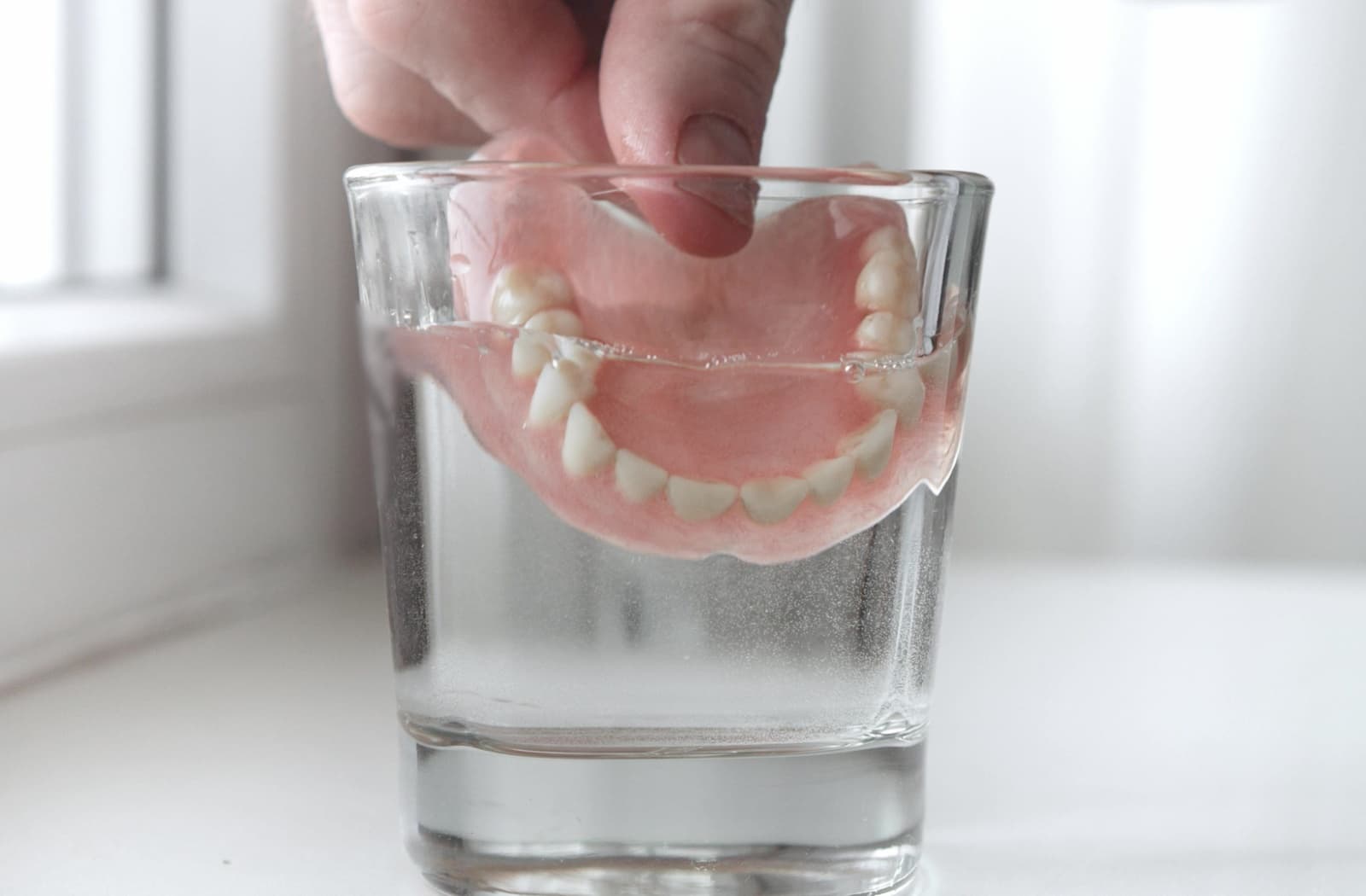 Dentures being placed into a glass of cleaning solution.