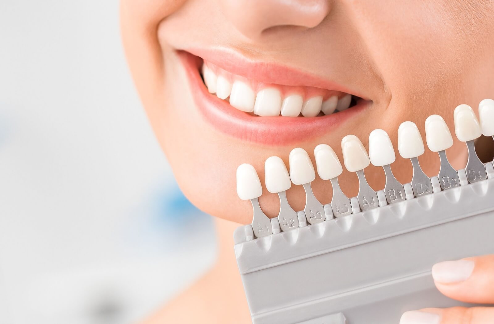 A picture of a person smiling and comparing a colour scale of teeth to their new dentures.