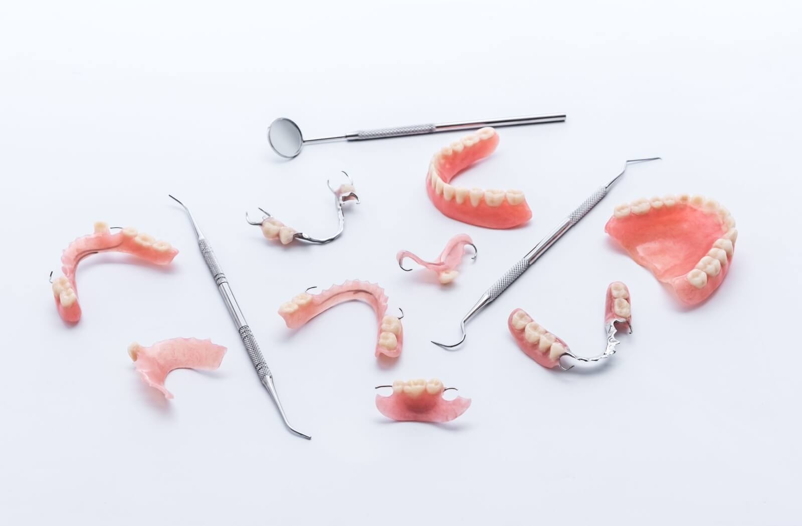 A number of sets of partial dentures of many varieties are displayed alongside some dental tools.